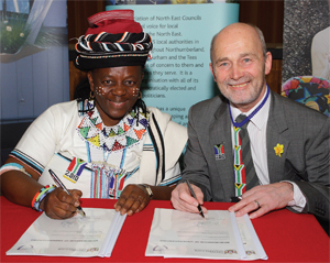 A man and woman sit behind a desk,  pretending to sign a documents