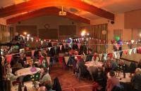 A photo of a village hall with tables of people sitting down