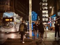 Buses passing and people crossing the street after dark