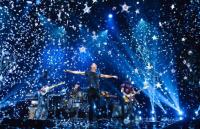 A photo of a band on stage surrounded by bright lights