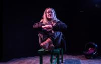 Photo of actor sitting on a bench, dimly lit stage, during in a monologue