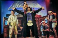 A pirate on stage performing Treasure Island in front of a ship prop and his crew