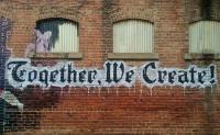 Graffiti on a brick wall reading 'Together We Create'