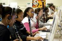 Young people with clarinets recording music on desktop computers