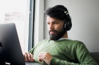 A man sitting with a macbook on his lap while wearing headphones