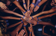 the bare arms of a group of mixed-race people stretching out hands on top of each other in a circle