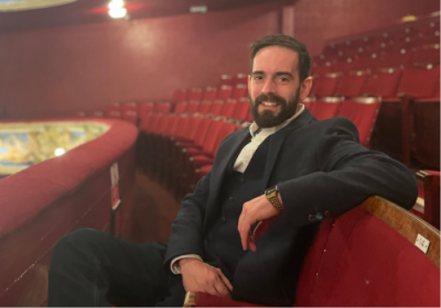 Graham McKnight sits in a theatre auditorium wearing a dark suit