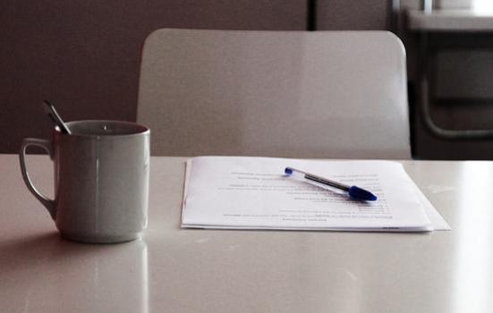 Photo of paper on a table with a pen and mug