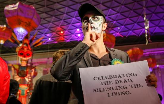 Face-painted man with sign: 'Celebrating the dead, silencing the living'