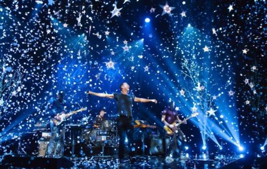 A photo of a band on stage surrounded by bright lights