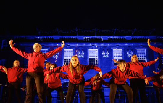 performers dance in front of a lit up building