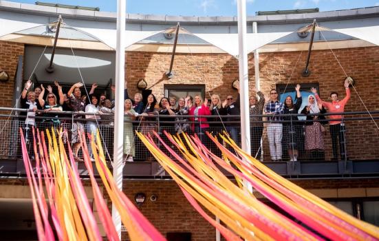 My Leeds 2023 Neighbourhood Hosts programme. People stood on a balcony waving and smiling.