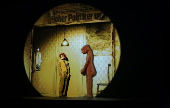 Performance of Golem. Person in clown makeup alongside 'Golem' – a creature crafted from clay. They are both stood on stage.