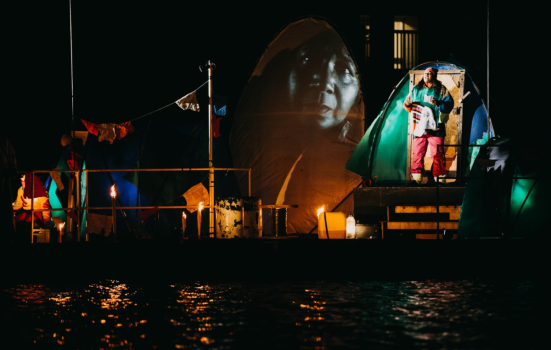 An actor stands in front of a tent surrounded by water