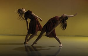 Two dancers leaning back and posing against a yellow background