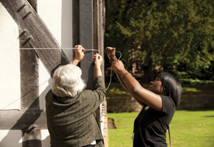 Two women standing next to a building holding up some string to the wall