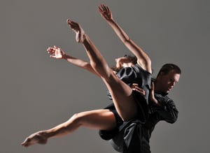 A male and a female dancer performing a lift - the male dancer is lifting the female dancer who has her arms and legs flung wide