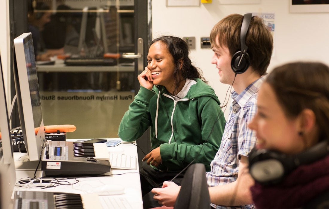 Three young adults working with a keyboard at a computer