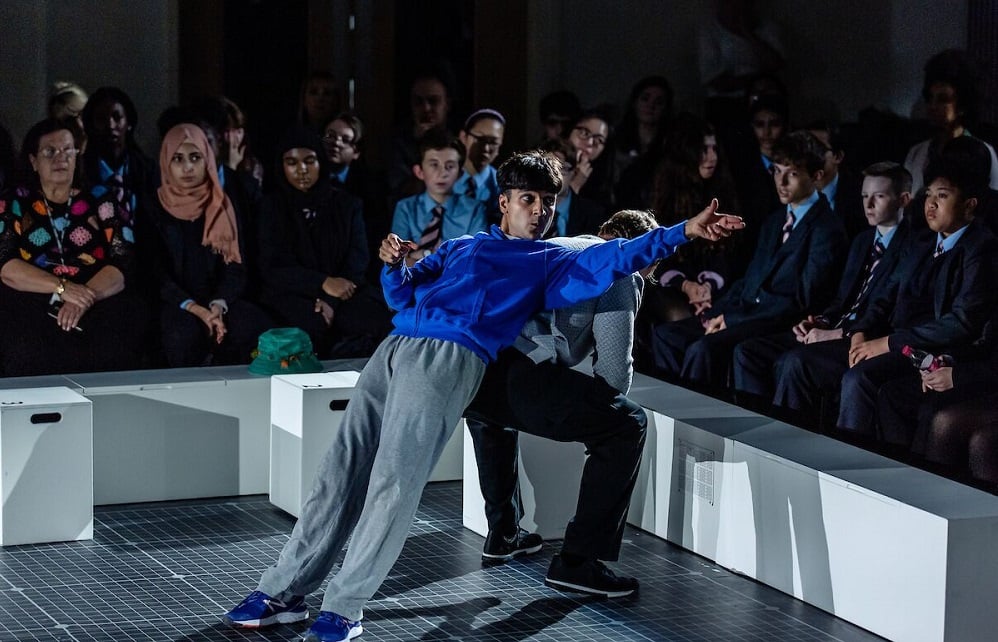 A photo of a young man on a stage leaning against another actor