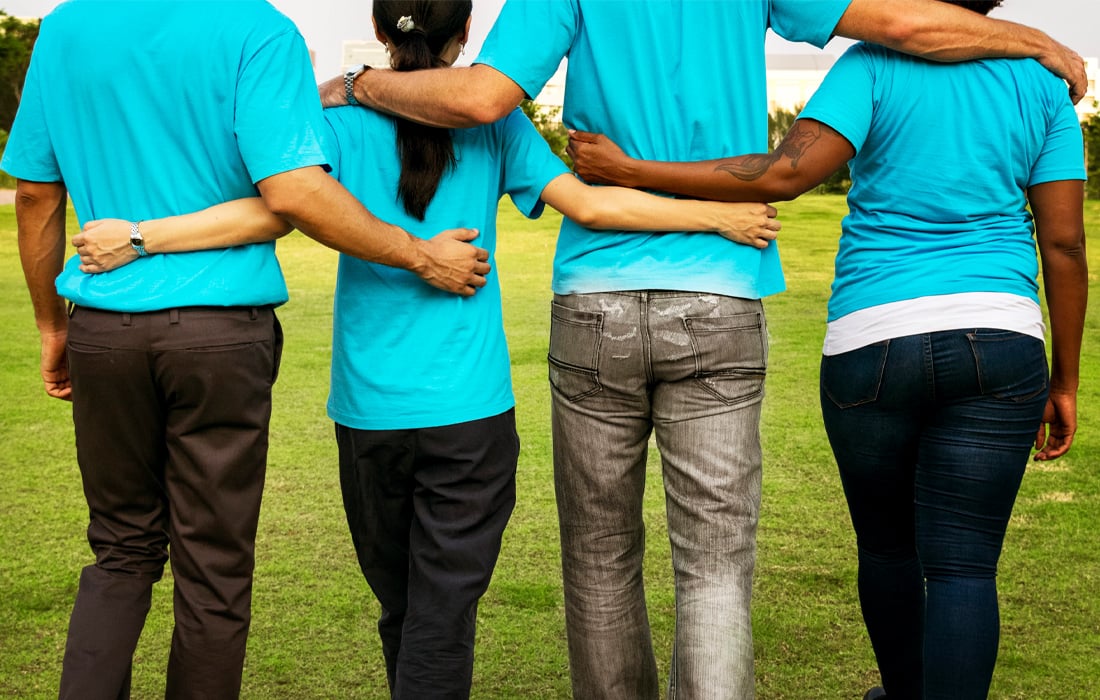 People from different ethnicities and genders linked arm in arm, photographed from behind