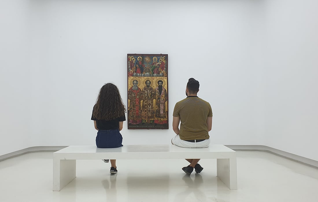 man and woman sitting on a bench looking at a painting in a gallery - view from behind the couple