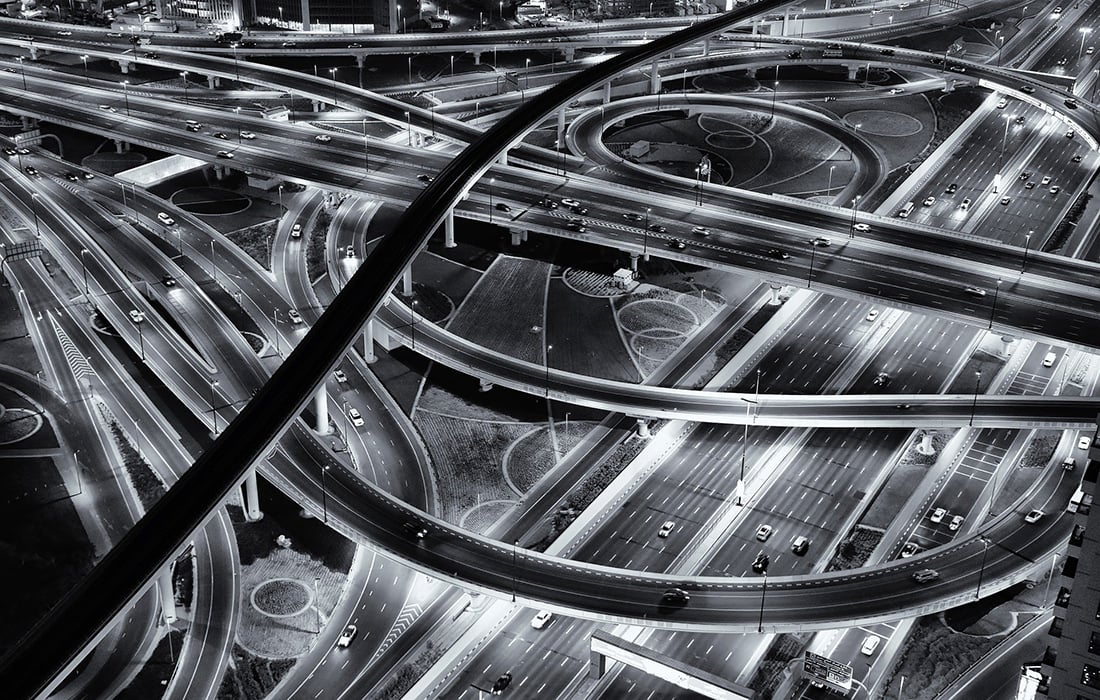 mono photograph showing an aerial view of a road network taken at night with cars visible on the carriageways