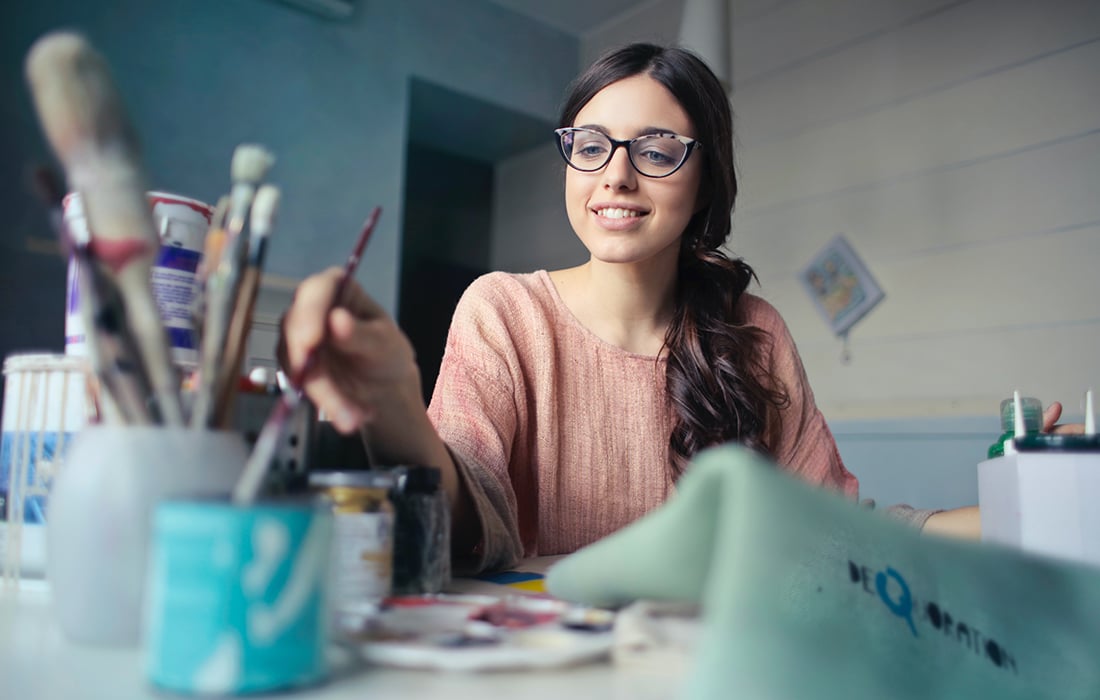 girl sitting at a desk with a paintbrush in hand