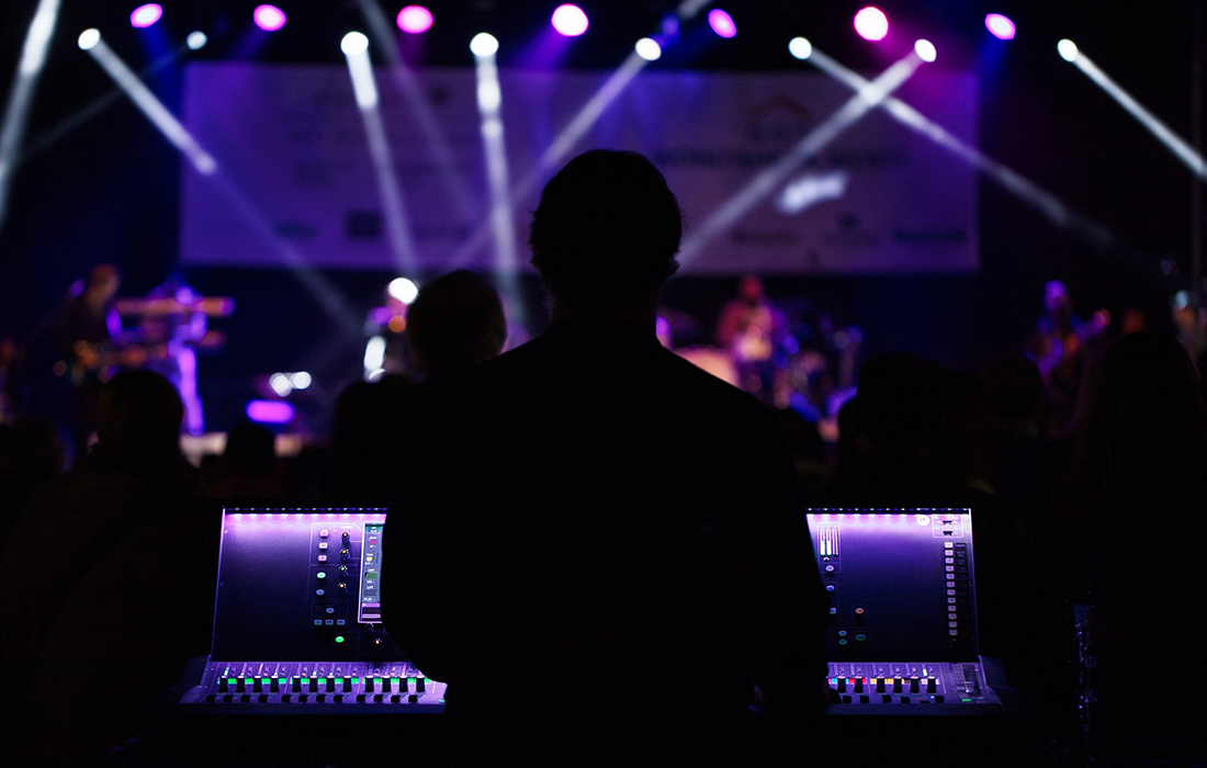 dark silhouette of a sound operator (taken from behind) in a theatre or music show with lights onto the stage