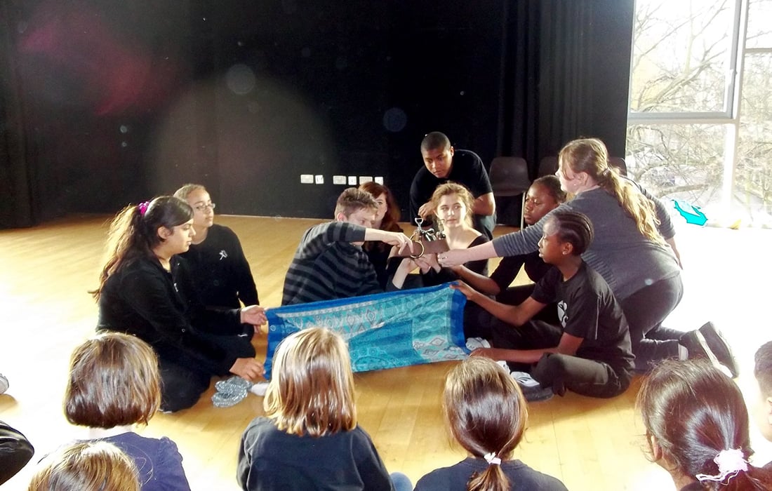 group of children sitting cross-legged in a studio holding a silk cloth and other props