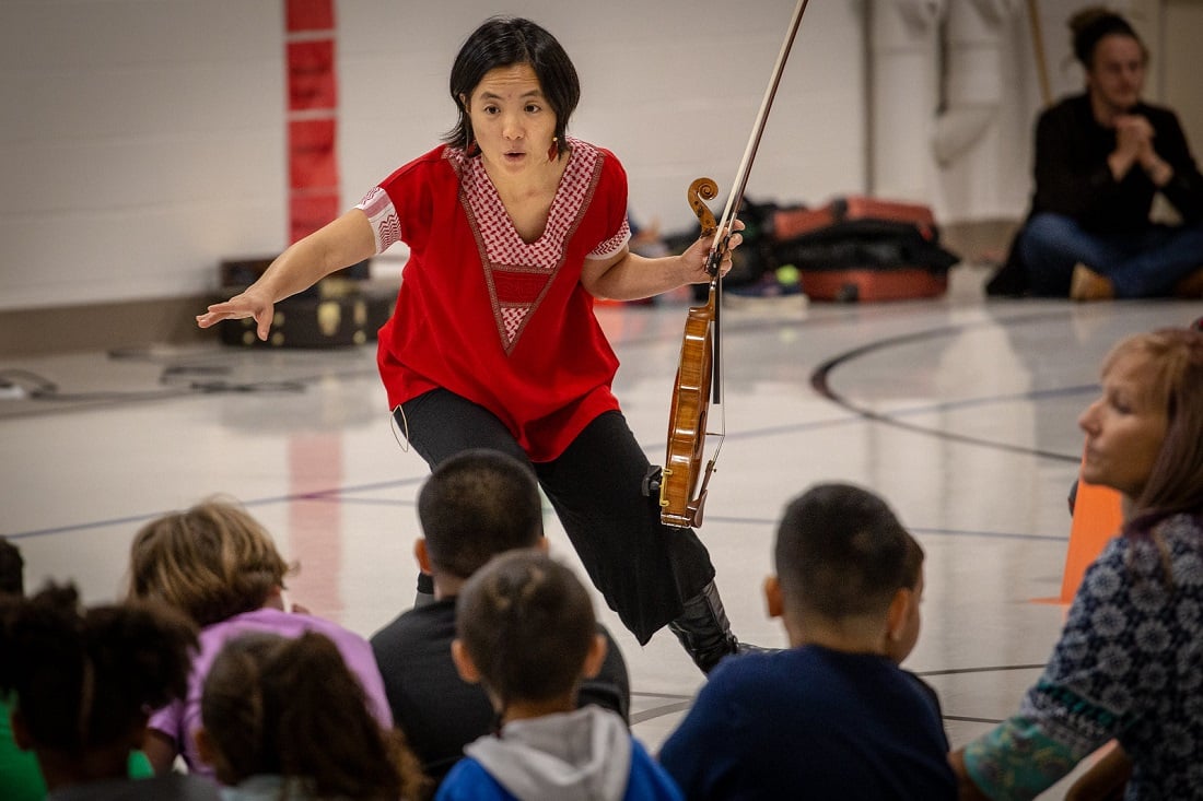 Woman with violin teaching young children in a school hall