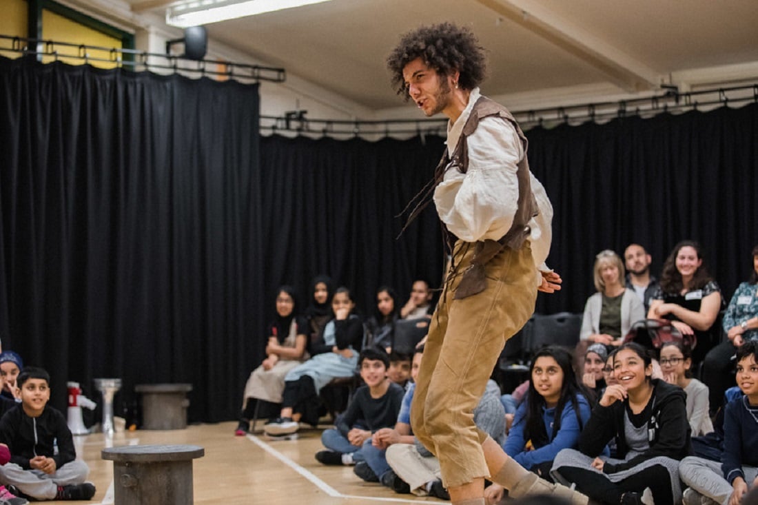 A man performing in a school gym surrounded by school children