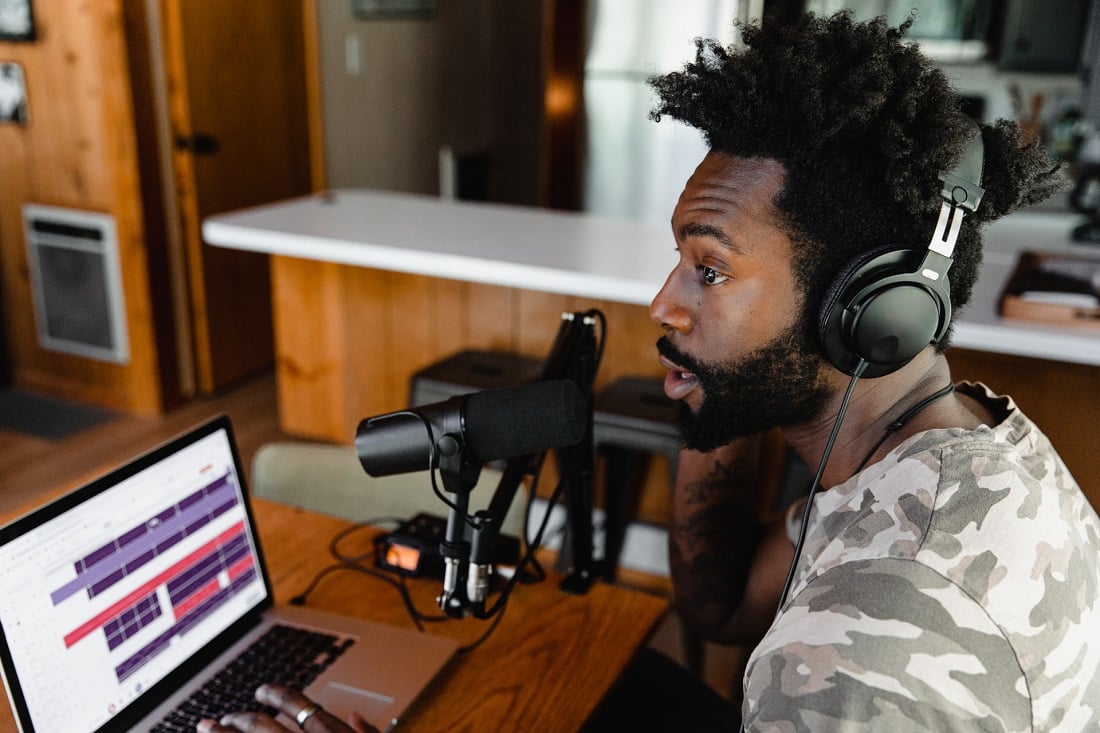 Man with headphones and microphone recording on a laptop