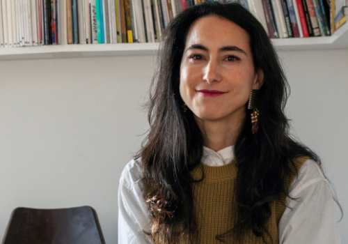 Portrait of Salma Tuqan smiling with bookcase behind