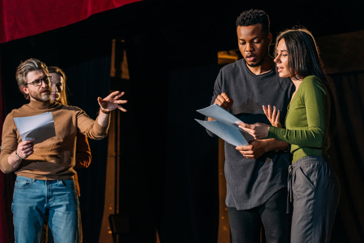 A theatre director watches an actor and actress rehearse lines on a theatre stage