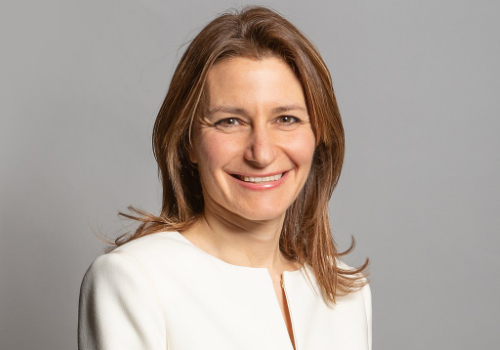 Lucy Frazer can be seen smiling at the camera while wearing a white top featuring a small 'V' cutout. She has short, light brown hair and is a white woman. Lucy Frazer is currently serving as the Secretary of State for Culture, Media & Sport.