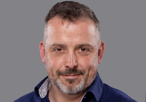 Steve Dimmick, Commercial Director, Awen Cultural Trust. Dimmick is a white man with short, brown hair, a brown/grey beard, and brown eyes. He wears a dark blue shirt, and is smiling at the camera. The background is grey.