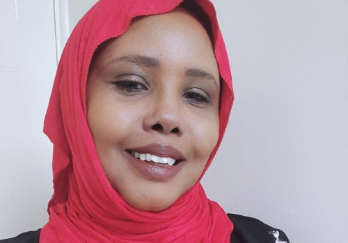 Kaltum Osman Rivers, Board Member of Sheffield's Utopia Theatre, is a Black woman who wears a pink hijab. She is taking the image herself, and smiling at the camera.