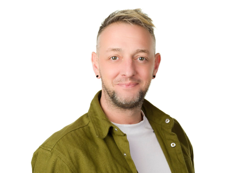 Adam Pownell, Executive Producer Zest Theatre. He wears a green shirt with a white t-shirt underneath. He has blonde hair, and wears black stud earrings. The background is white.