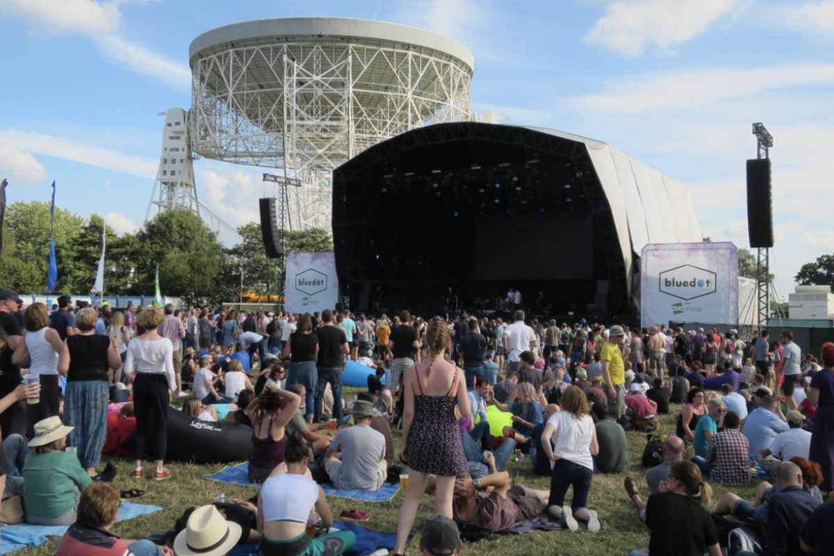 an audience waits for an act to start at Bluedot main stage, with a telescope behind the stage