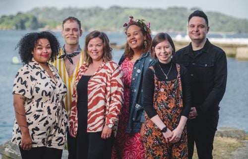 (L to R): Malaika Kegode, Tom Jackson Greaves, Sara Rhodes, Bee Jarvis, Natasha Pavey, and John Haidar, June 2023. The six new appointments are stood outside on grass in front of the sea in Plymouth.