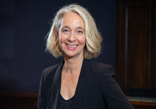 Anna Farthing, incoming CEO, New Theatre Royal Portsmouth. She has short blonde hair and wears pink lipstick, a black blazer and black top/dress. She is photographed sat down and smiling.