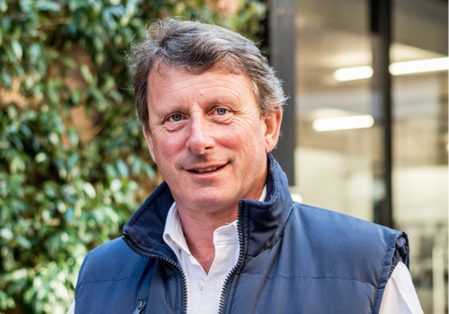 Headshot of Edward Benyon with a blurred background, he has grey hair and wears a navy gilet and white shirt.