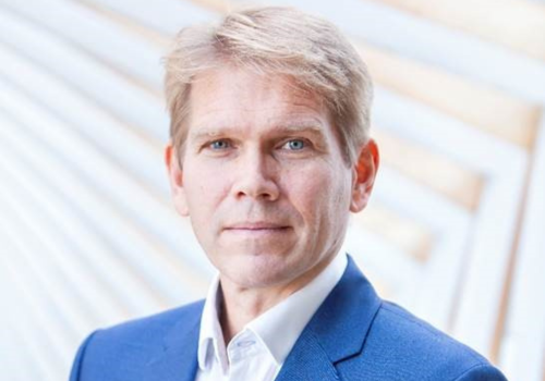 Headshot of Christopher Powney. He is a white man with blonde hair and green eyes. He wears a blue suit and white shirt.