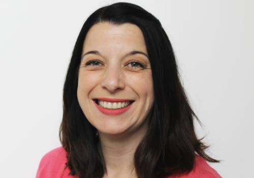 A headshot of Jo Cornish, she has straight dark hair and wears a pink top