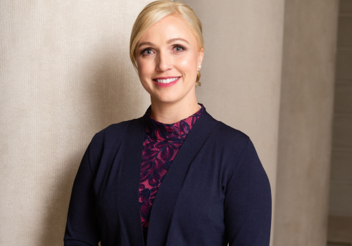 Melissa Buron, a white woman with blonde hair smiles at the camera, she wears a navy blue and purple top.