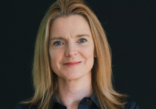 A headshot of Vicky Cheetham, a white woman with blonde hair infront of a black background