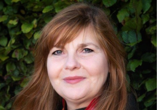 A headshot of Emma Nicolson - a white woman with long auburn hair