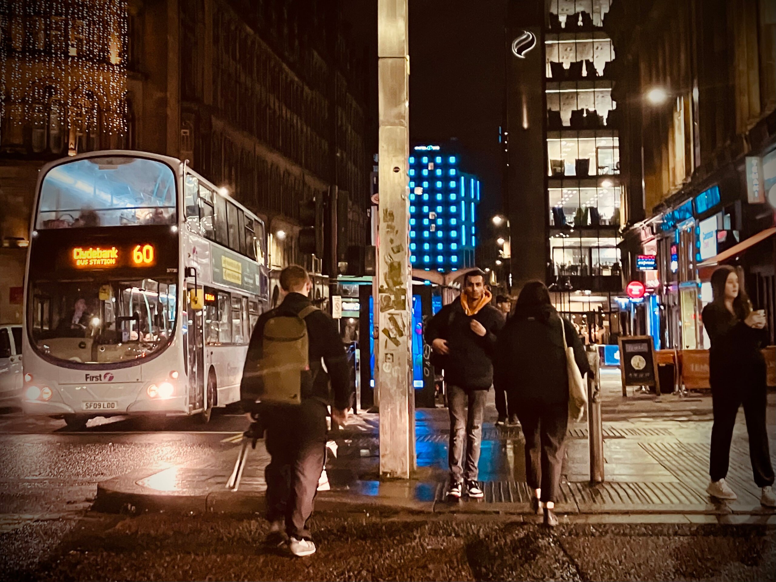 Buses passing and people crossing the street after dark